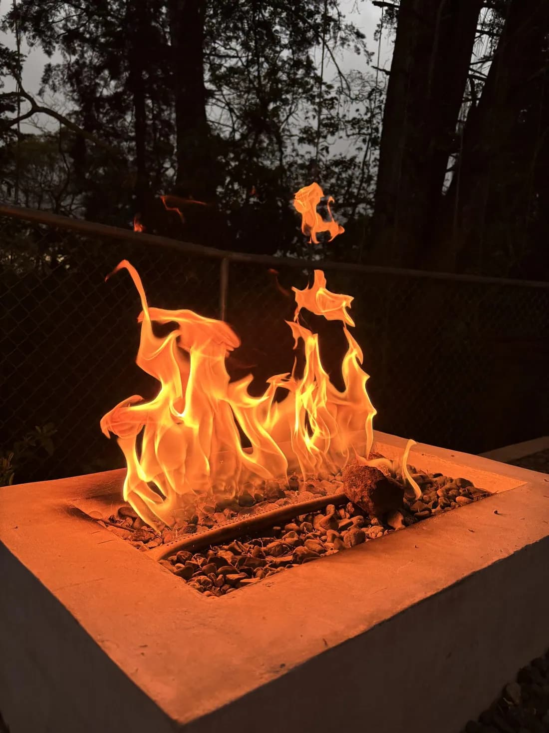 A gas fire feature burning in a squared concrete surround at dusk